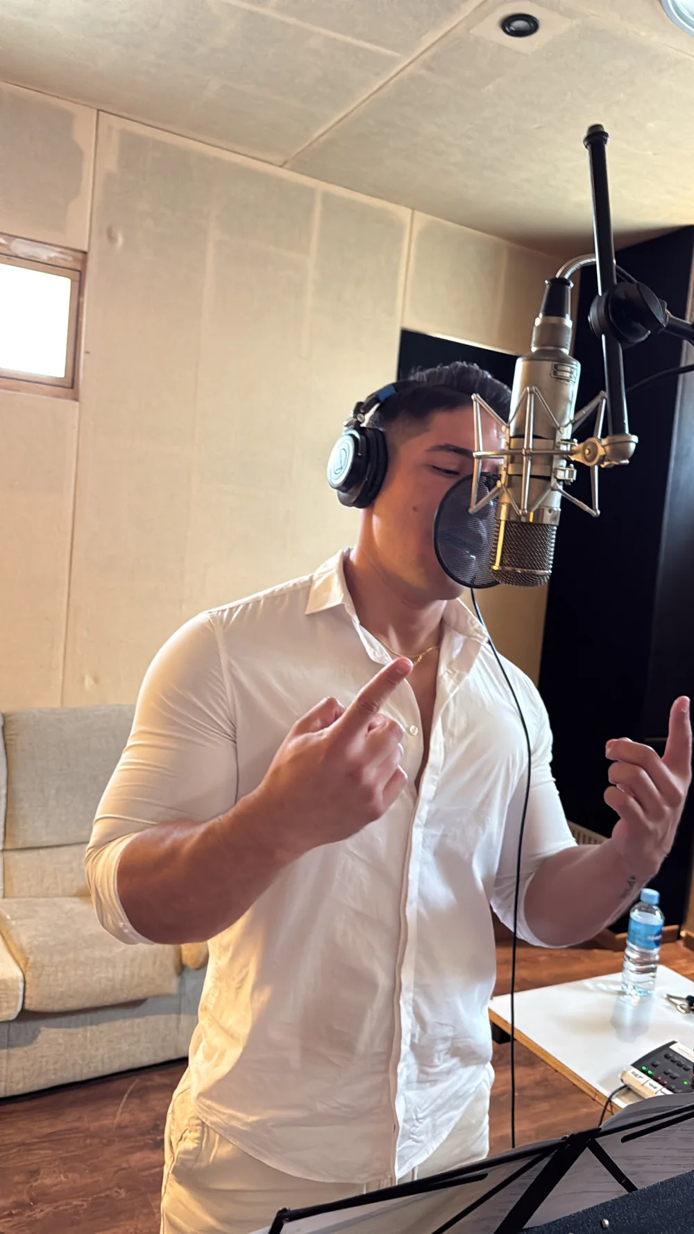 GIAN cantando con camisa blanca y auriculares en el estudio